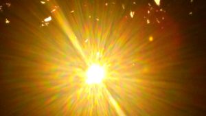 Close-up of a natural peep hole in a rustic tree trunk with bright, golden sunbeams exploding through the center, creating a dramatic and radiant light leak effect across the entire image.