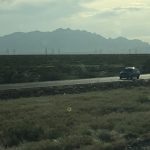 A highway ahead with a massive mountain visible in the distance on the left side under the sky.