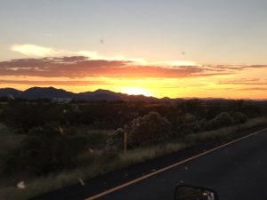 A beautiful gold and orange sunset casting a radiant glow over a majestic mountain range beneath dark, dramatic clouds.