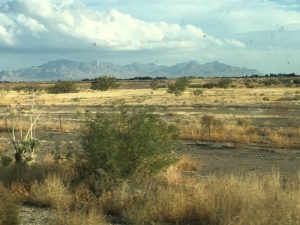 A beautiful mountain range standing tall in the far background behind a wide open field along a scenic West Coast journey.