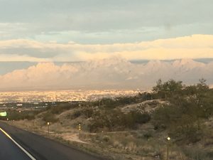 A striking highway drive at dusk looking toward majestic mountains in the distance under a beautiful peach sky.