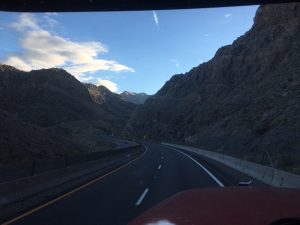 A striking highway view enclosed by massive solid rock mountains on either side, with a piece of a red 18-wheeler truck moving forward down the pass.