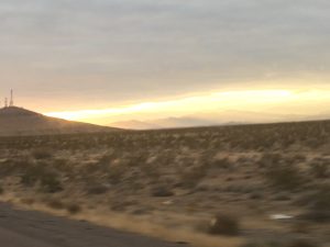 A striking photograph of West Coast mountains in the distance under a low gold sunset with a dramatic mix of colored rain clouds