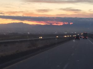 A breathtaking highway view at dusk showing a vibrant sunset resting on top of a dark cloud with mountains in the background.