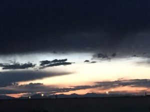 Dramatic black clouds hovering heavily in the sky with a small mist of sunlight breaking through over a majestic mountain range standing steady in the far distance.