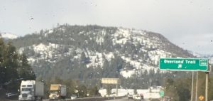 A beautiful close-up photograph of a huge mountain with soft snow falling lightly over its rugged peaks and green evergreen trees.