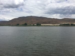 A natural scenic view of a wide, expansive lake with gentle rippling water leading to a single large mountain standing far off in the background distance under a soft sky.