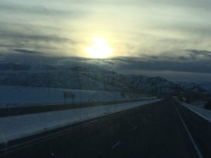 A high-quality, inspiring landscape photograph of a bright, radiant sun peaking over the dark silhouette of a rugged mountain range at dawn, casting warm golden rays across a dark sky.
