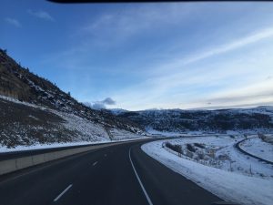 A beautiful photo looking down a peaceful winter road that stretches forward toward a gentle curve, with a clean layer of fresh snow resting on the ground along the journey.