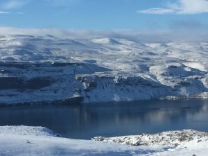 A stunning view across a peaceful lake looking at a massive, singular snow-capped mountain standing majestically on the opposite shore under a clear sky.