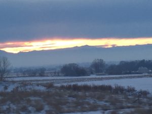 A gorgeous photo capturing a brilliant gold and orange sunset peeking out perfectly in between low dark clouds above and a majestic mountain range below.