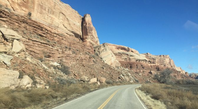 A striking landscape photograph looking down a curved asphalt highway that winds gracefully between two massive, towering rock mountains.