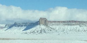 A beautiful photograph of a massive, solid rock mountain with snow on its peaks under a vast sky, with no pavement or roads visible.