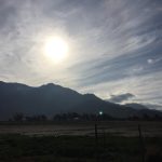 A beautiful photo looking across a wide, open field stretching forward to a majestic rock mountain range rising under a grand sky in the far background.