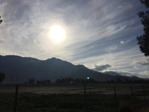  A beautiful photo looking across a wide, open field stretching forward to a majestic rock mountain range rising under a grand sky in the far background.
