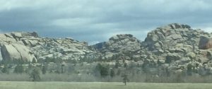 A high-quality, dramatic landscape photograph of a rugged rock mountain range under dark, swirling stormy skies, highlighting a unique and beautiful natural rock formation in sharp focus.