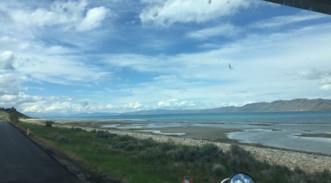 A peaceful vehicle parked on the side of a still body of water with a line of mountains under a clear sky with no sun