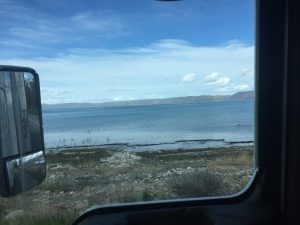 A scenic view of a quiet body of water with small mountains sitting along the horizon in the far distance under a clear sky.