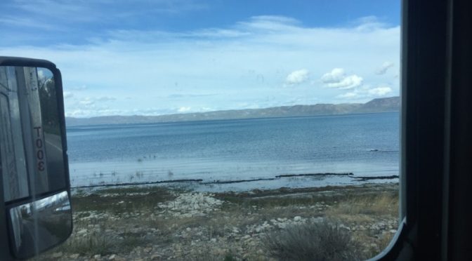 A scenic view of a quiet body of water with small mountains sitting along the horizon in the far distance under a clear sky.