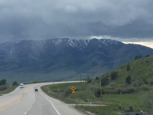 View from the front of an 18-wheeler truck driving toward distant mountains under a dark, dramatic evening sky.