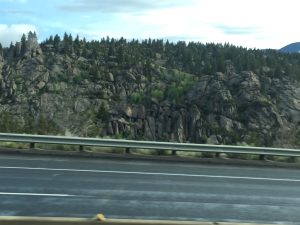  A beautiful photograph of a winding road running past a small mountain covered in large gray boulders and green evergreen trees
