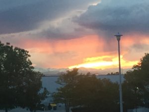 A breathtaking view of a vibrant orange and gold sunset casting its final twilight glow over a major mountain range standing steady in the far distance under dark clouds.