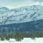 A serene view of a snow-capped mountain range under a clear sky, with a crisp, detailed close-up of pure winter snow filling the right-hand side.