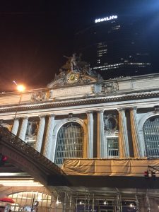 An architectural view of Grand Central Terminal at night with the massive MetLife building towering directly behind it in midtown New York City.
