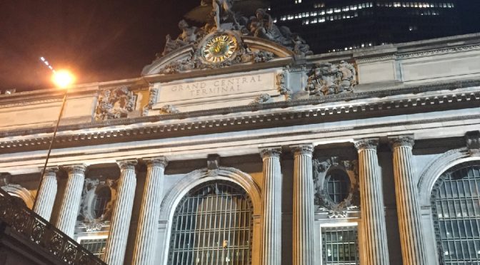 An architectural view of Grand Central Terminal at night with the massive MetLife building towering directly behind it in midtown New York City.