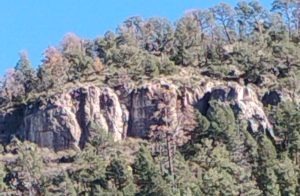 A pristine close-up of a massive rock mountain range covered in trees under a clear sky.