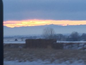 A soft focus, abstract perspective of a brilliant sunset glowing warmly in the narrow space between dark storm clouds above and a silhouetted mountain ridge along the horizon line