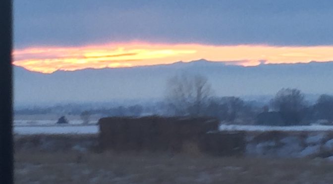 • A soft focus, abstract perspective of a brilliant sunset glowing warmly in the narrow space between dark storm clouds above and a silhouetted mountain ridge along the horizon line.