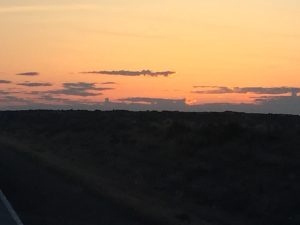 A dramatic desert sunset casting a deep, low glow beneath heavy, dark twilight clouds stretching across the wide horizon landscape.