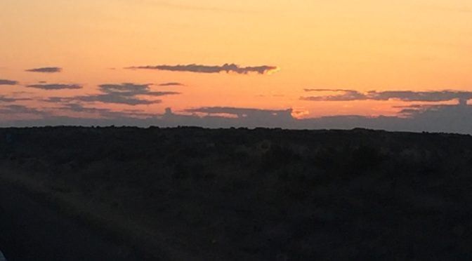 A dramatic desert sunset casting a deep, low glow beneath heavy, dark twilight clouds stretching across the wide horizon landscape.